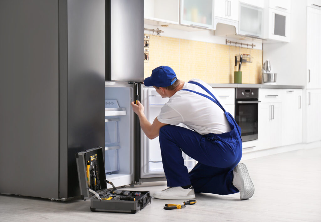 Male technician with screwdriver repairing refrigerator in kitch